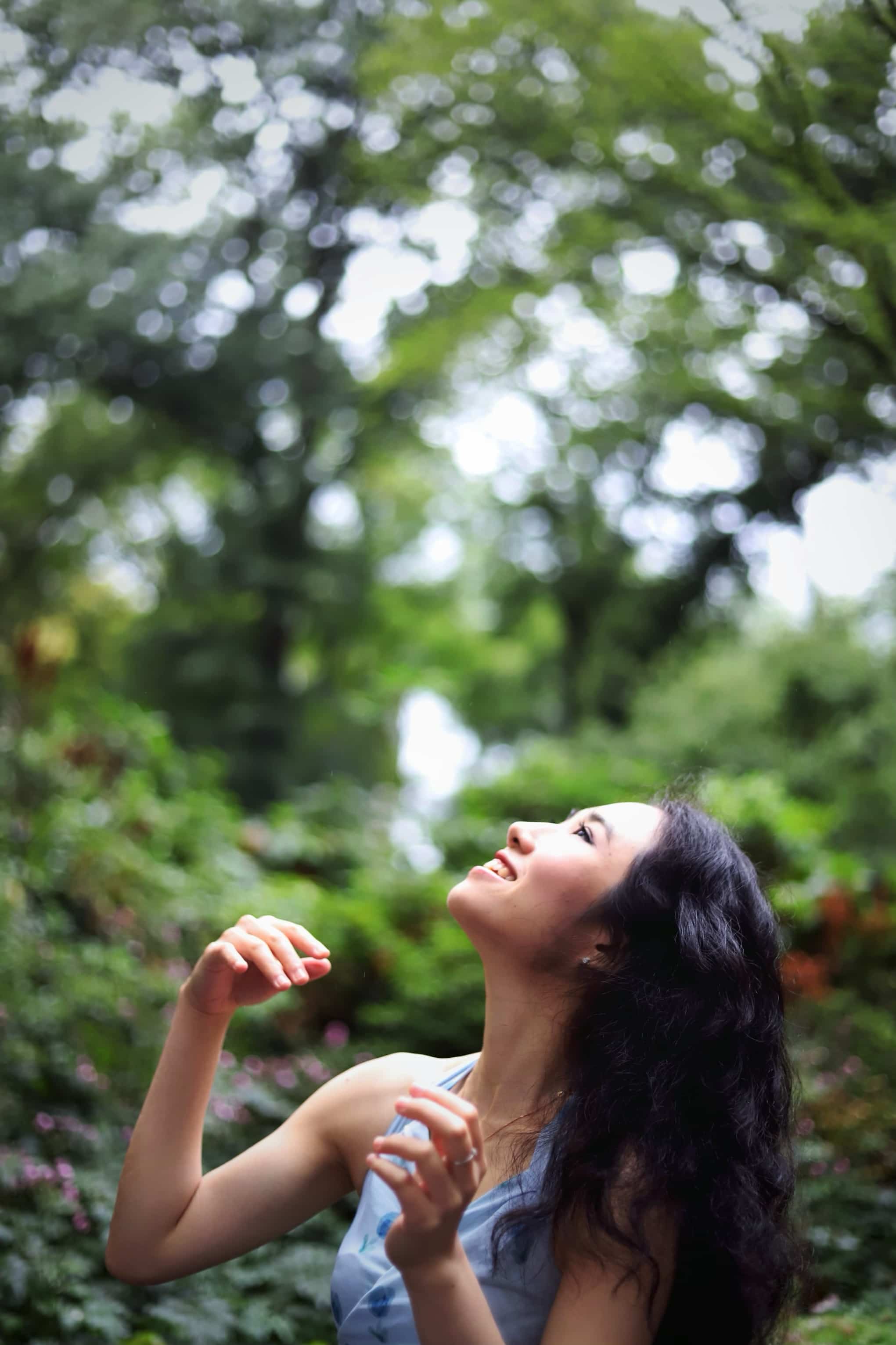 Minyi Zhang in a blue dress looking upward in a leafy garden.