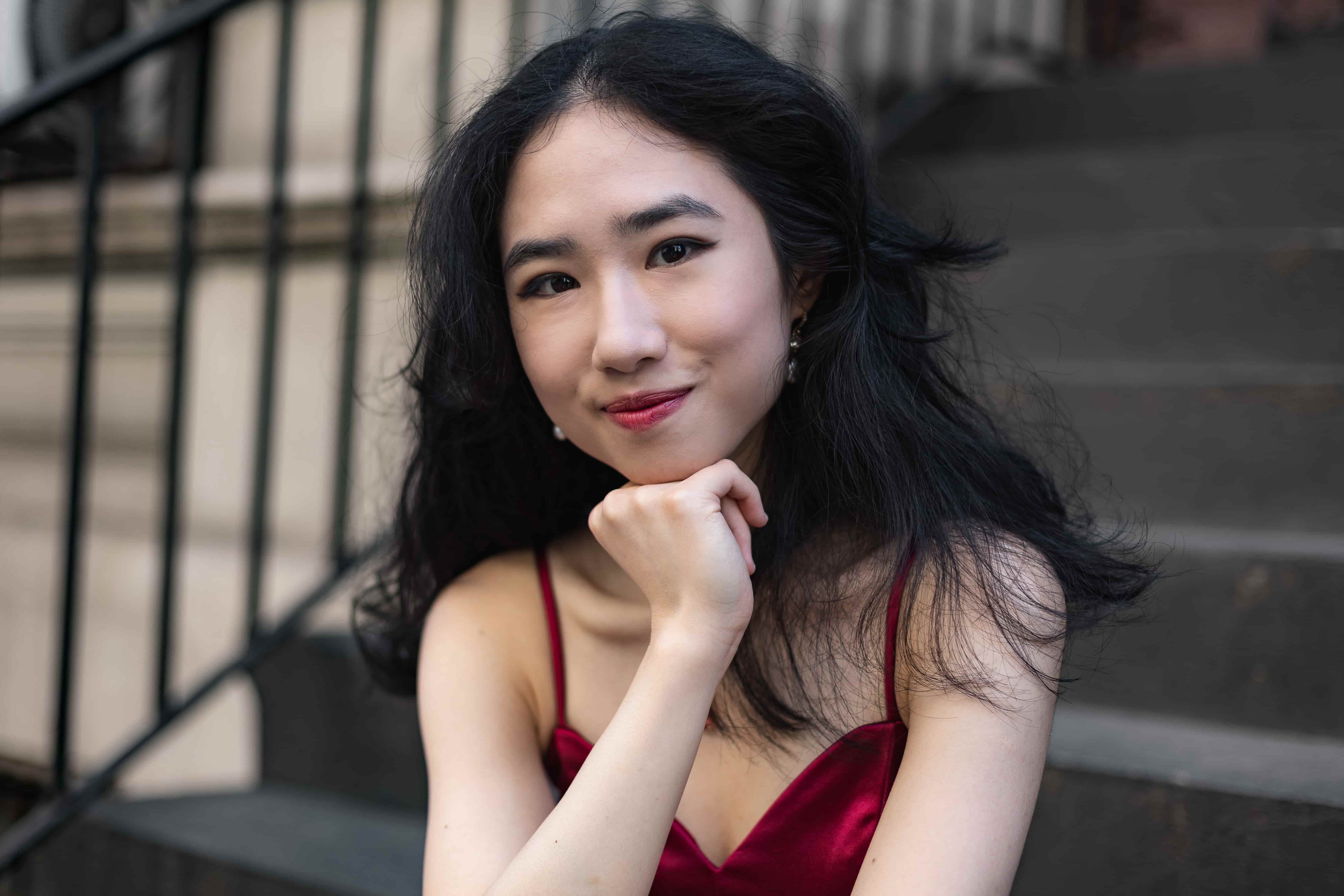 Minyi Zhang in a red dress seated on brownstone steps, resting her chin on her hand.